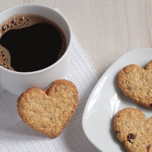 Close-up of coffee and oatmeal cookies in the shape of a heart on a light table
